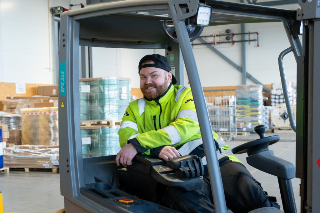 Foto av mann i arbeidstøy som sitter i truck og smiler til kamera